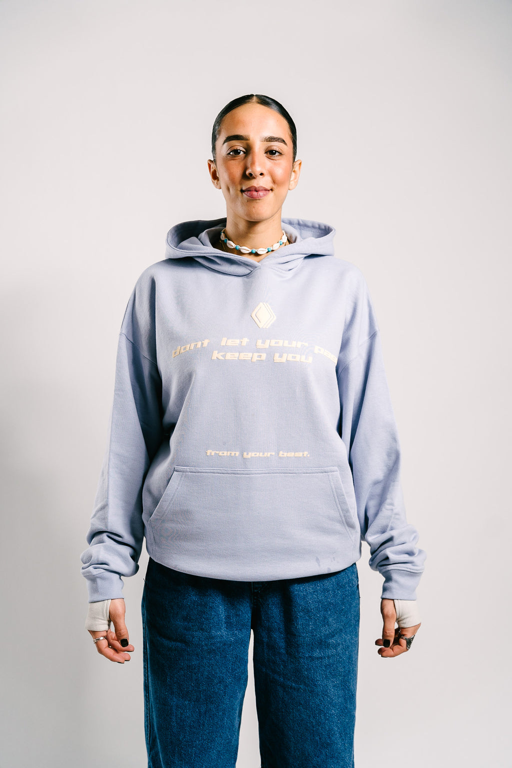 Person trägt einen hellblauen Unisex-Hoodie mit dem Markenlogo 'BAKLAVA' auf der Brust. Der Hoodie hat eine Drop-Shoulder-Passform, ist leicht oversized und besteht aus schwerer French Terry Baumwolle für Langlebigkeit und Komfort. Der Schriftzug auf dem Hoodie lautet 'don't let your past keep you' in größerer Schrift, mit 'from your best' in kleinerer Schrift darunter. Inspiriert von Kendrick Lamar’s Song 'Die Hard'.