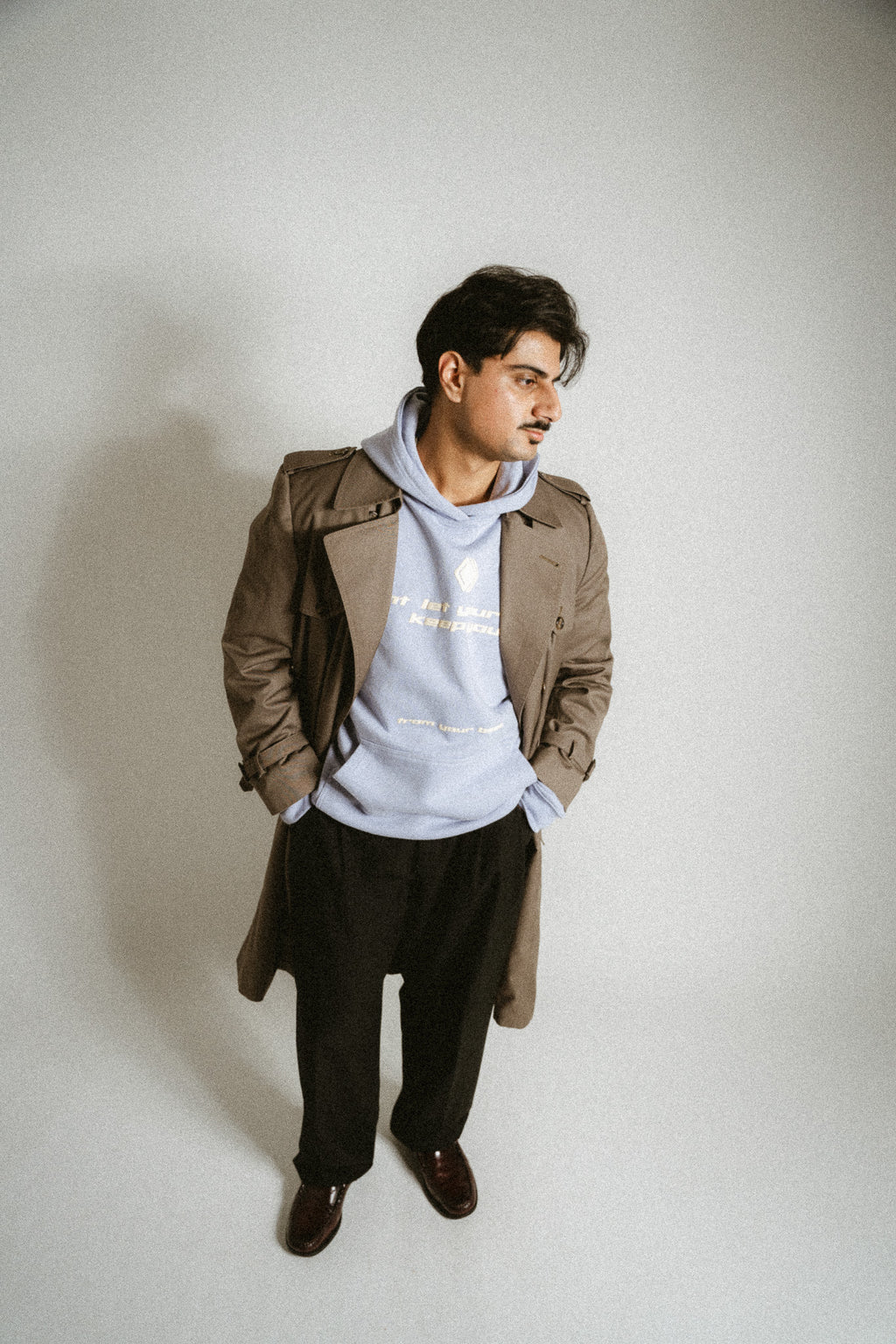 Person trägt unter einem Mantel einen hellblauen Unisex-Hoodie mit dem Markenlogo 'BAKLAVA' auf der Brust. Der Hoodie hat eine Drop-Shoulder-Passform, ist leicht oversized und besteht aus schwerer French Terry Baumwolle für Langlebigkeit und Komfort. Der Schriftzug auf dem Hoodie lautet 'don't let your past keep you' in größerer Schrift, mit 'from your best' in kleinerer Schrift darunter. Inspiriert von Kendrick Lamar’s Song 'Die Hard'.