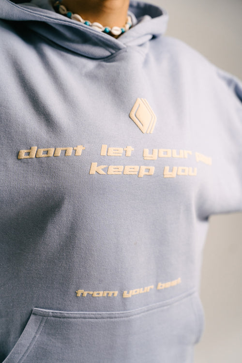 Nahaufnahme eines hellblauen Unisex-Hoodies mit dem Markenlogo 'BAKLAVA' auf der Brust. Der Schriftzug lautet 'don't let your past keep you' in einer größeren Schrift, gefolgt von 'from your best' in kleinerer Schrift am unteren Rand des Hoodies. Der Hoodie besteht aus schwerer French Terry Baumwolle mit doppelten Nähten, die für Langlebigkeit und Komfort sorgen. Inspiriert von Kendrick Lamar’s Song 'Die Hard'.